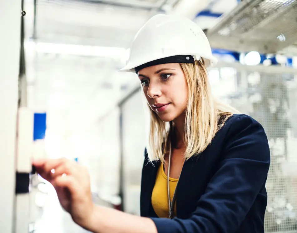 Woman in a white hard hat inspecting an item on the wall